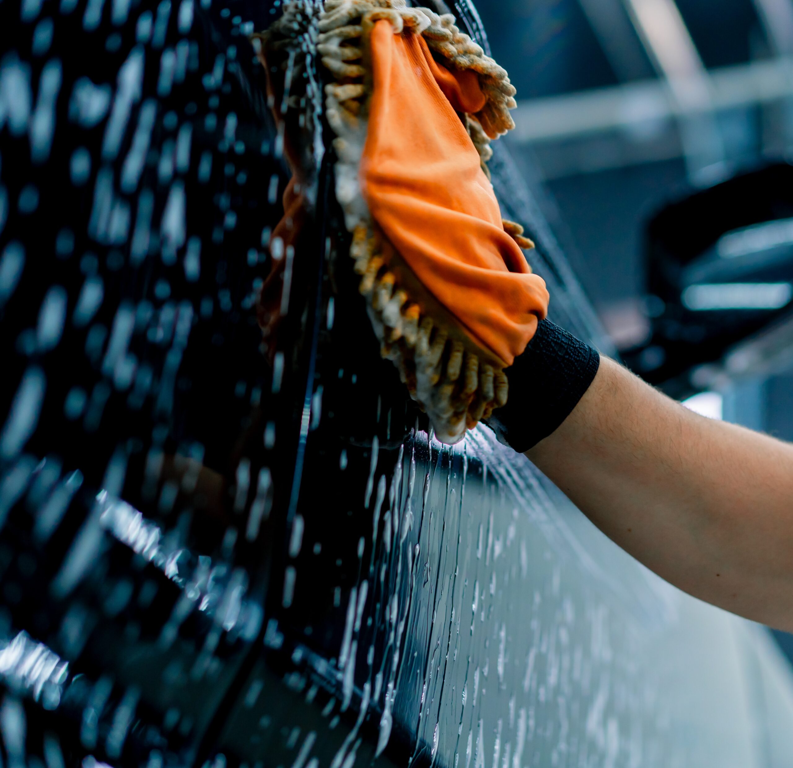 Close-up of a car wash worker using a microfiber cloth to wash black luxury car with car wash shampoo