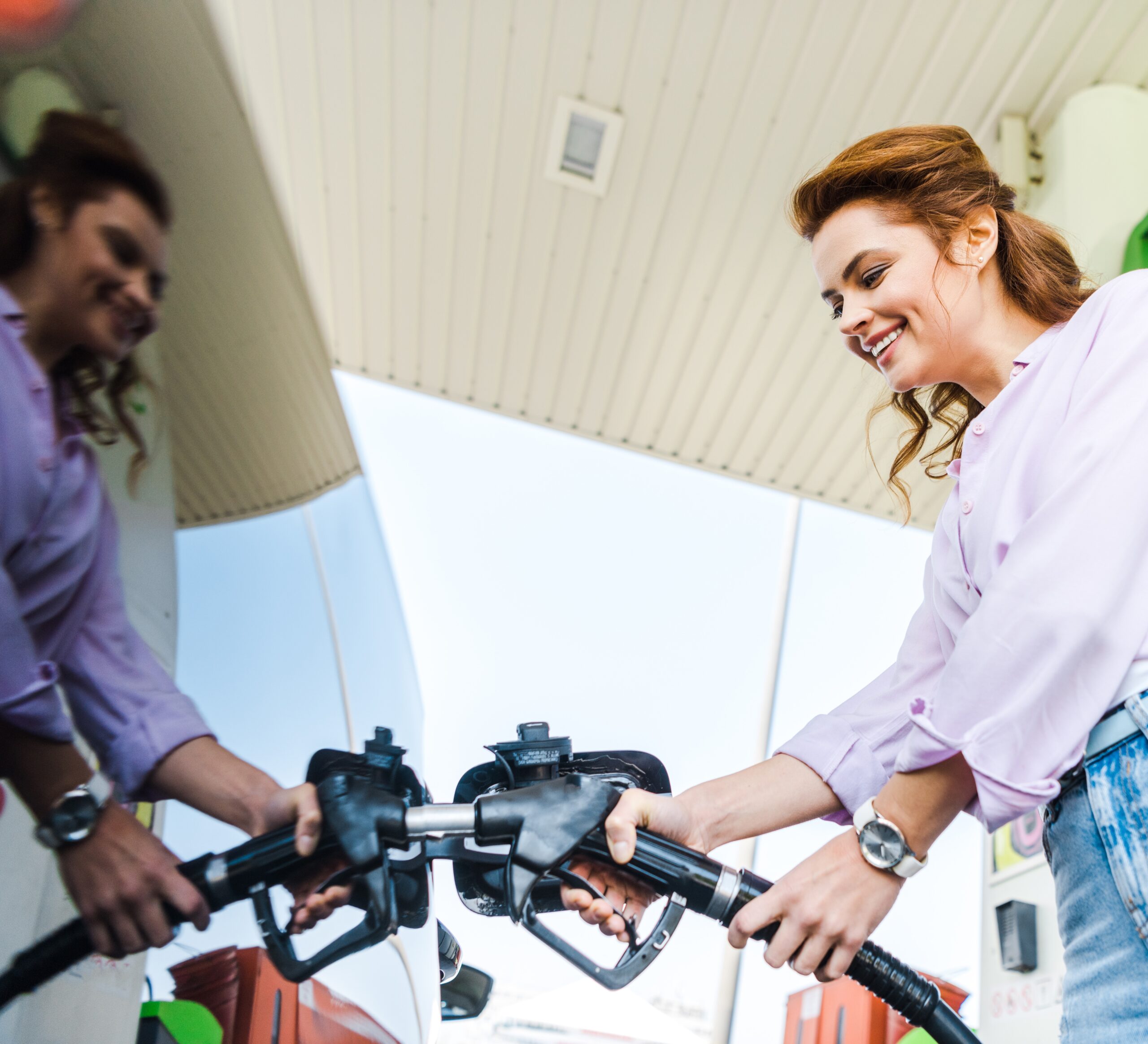 low angle view of happy woman holding fuel pump while refueling car with benzine